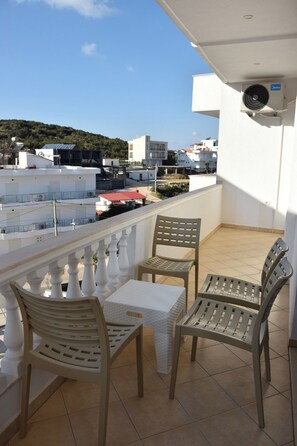 A balcony with a table and two chairs, overlooking a residential area with buildings and a hill. - Captain's Residence (Ksamil)