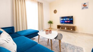 A modern living room with a blue sofa, a small white table, and a flat-screen TV mounted on the wall. - Captain's Residence (Ksamil)