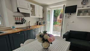 A compact living space with a kitchenette, a dining area with a checkered tablecloth, and a dark-colored sofa. - Casa Pitturini comfortable apartment in quiet area 500 m from the sea (Marciana Marina)