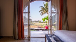 A bedroom with a large bed, a view of a garden, and a palm tree outside. - Lavender Villa by Ebony Stays – Peaceful 3 BHK Getaway in Nashik (Gangavhare)