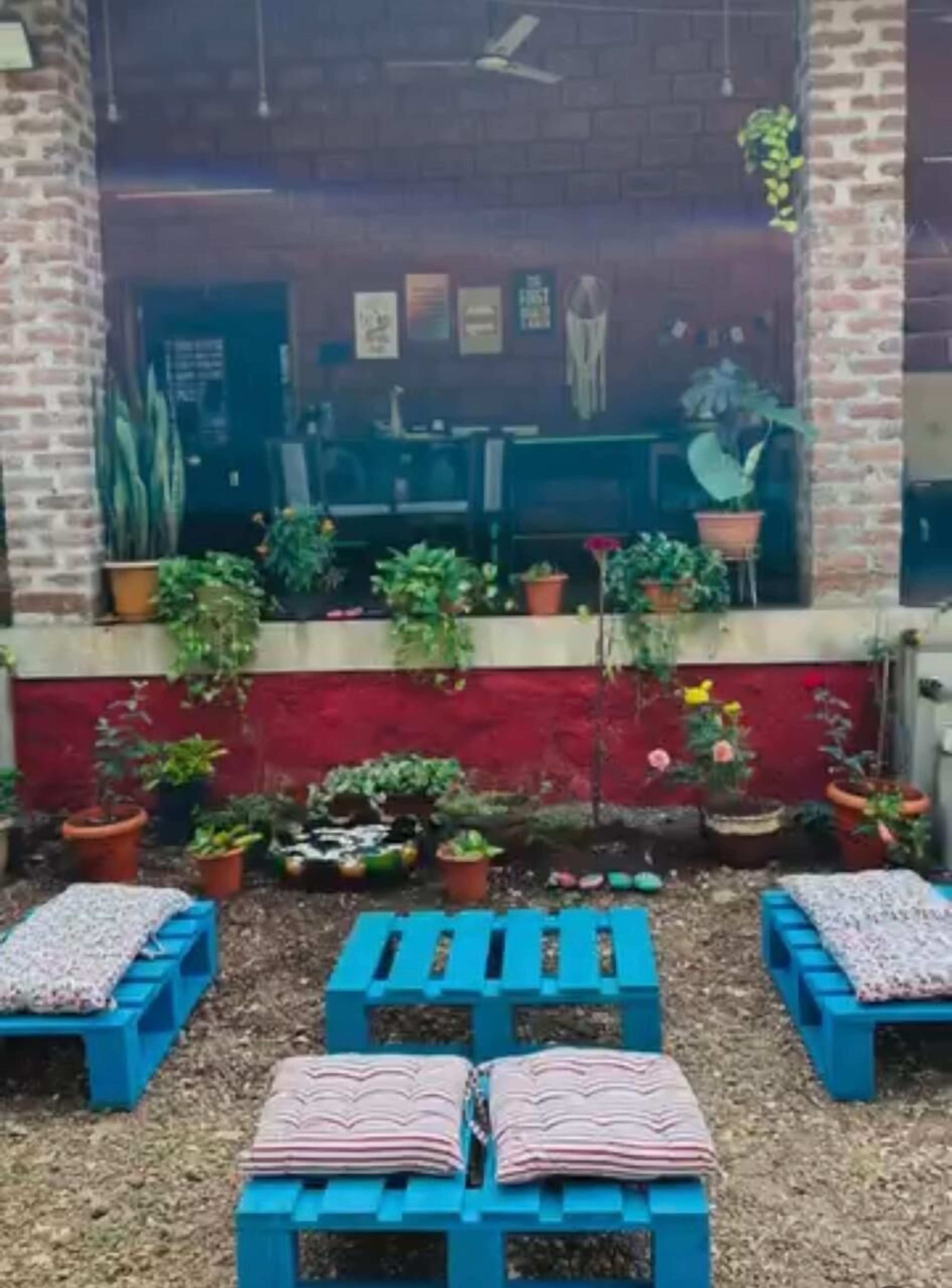 A covered outdoor seating area with blue benches and potted plants.