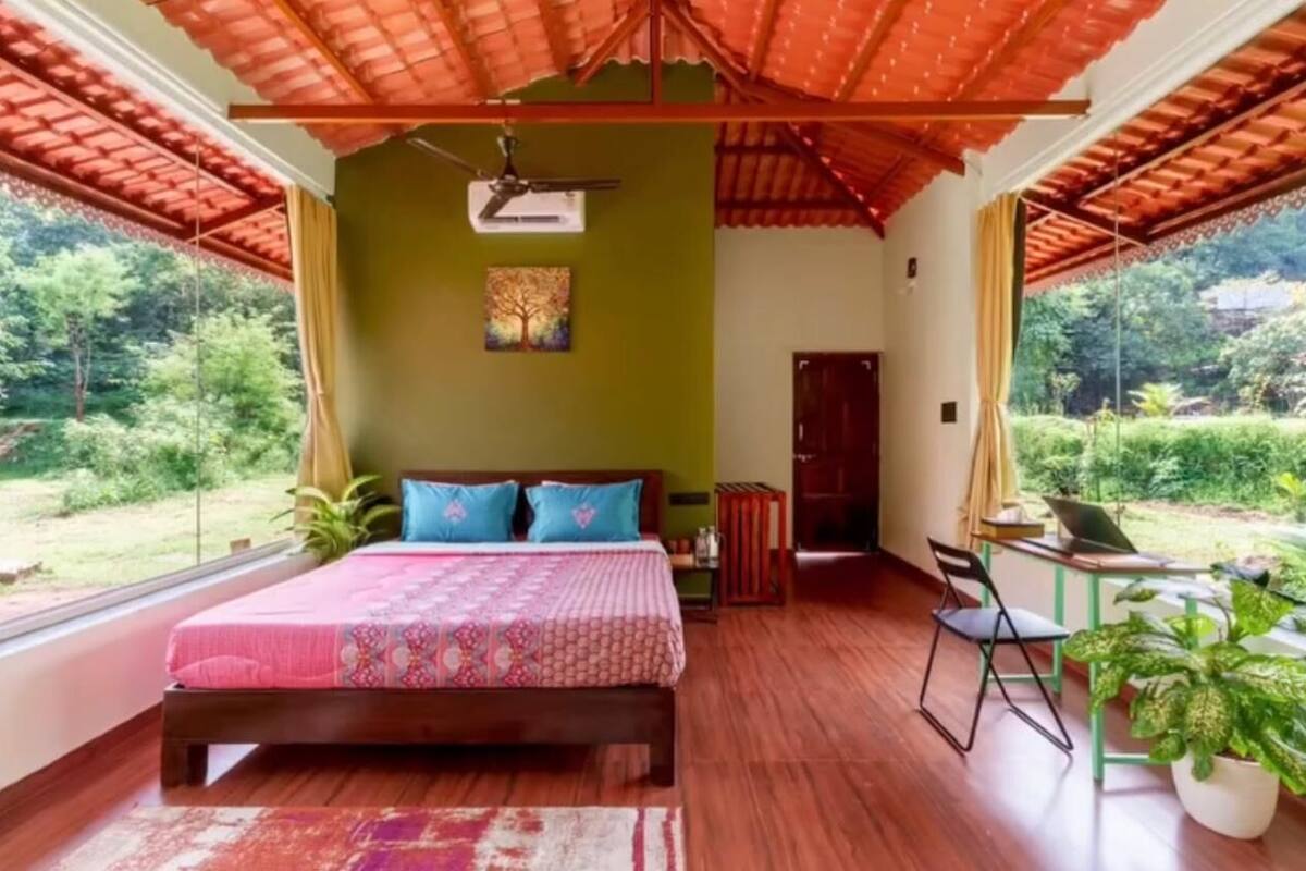 Ein Schlafzimmer mit Bett, Schreibtisch und Stuhl, einem Deckenventilator und einem Fenster mit Blick ins Grüne.
