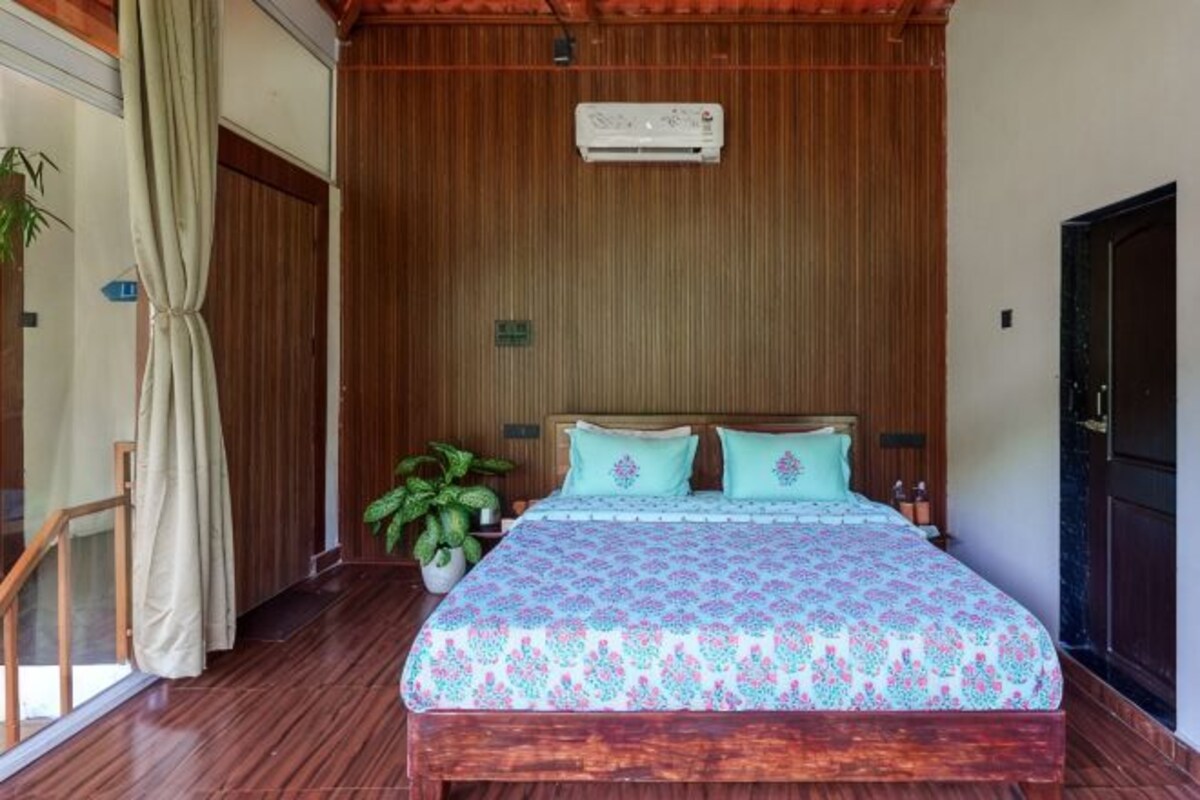 Un dormitorio con techo de madera, una cama con ropa de cama estampada, una planta en maceta y una puerta corredera.