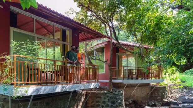 A two-story building with a balcony, stone foundation, and a view of a stream. - LeafyDen Forest Cottages by Nature Hill (Murud)
