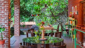 An indoor dining area with round tables and chairs, a ceiling fan, and a brick wall. - LeafyDen Forest Cottages by Nature Hill (Murud)
