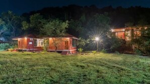 A small, rustic cabin with a wooden exterior and a porch, surrounded by a grassy area and trees. - LeafyDen Forest Cottages by Nature Hill (Murud)
