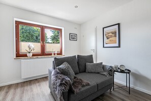 Una sala de estar moderna con un sofá gris, una mesita auxiliar, un cuadro enmarcado en la pared y una ventana con persianas.