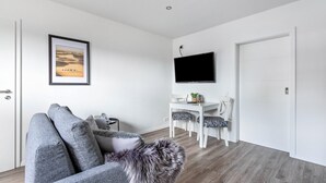 En moderne stue med sofa, spisebord og et TV ophængt på væggen.