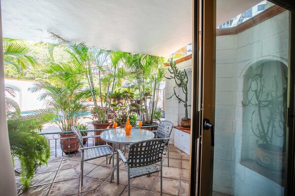 A patio with a round table, chairs, potted plants, and a glass door. - Casa Robalo (Puerto Vallarta)