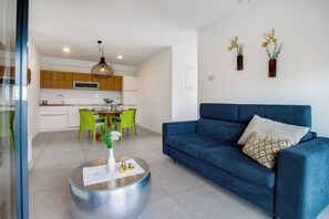 Uma sala de estar moderna com um sofá azul, uma mesa de centro redonda e uma área de jantar com cadeiras verdes.