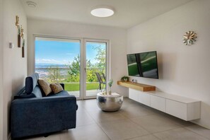 A modern living room with a sofa, a round side table, a flat-screen TV, and a sliding glass door leading to a balcony. - La Lita. Panoramic Sea View- Fast Wi-Fi -Free Parking (Šmarje pri Kopru)