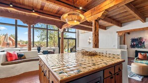 A spacious living area with a large wooden table, a built-in oven, and a cozy seating area with cushions. - Modern Adobe Masterpiece | Private Hot Tub | Rooftop Deck (Santa Fe)