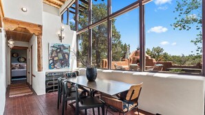 A dining area with a large window, a wooden ceiling, and a painting on the wall. - Modern Adobe Masterpiece | Private Hot Tub | Rooftop Deck (Santa Fe)