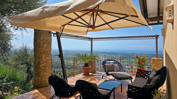 Eine überdachte Terrasse mit Gartenmöbeln und einer Pergola, mit Blick auf die Landschaft.