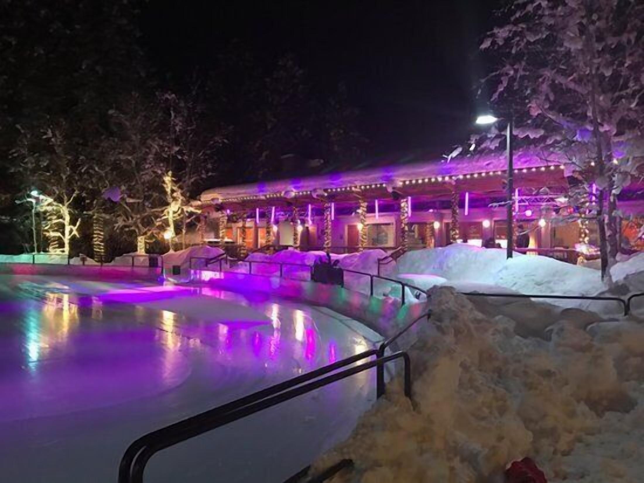 Vista nocturna de un hotel con zona de piscina iluminada por luces moradas.
