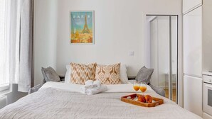 A hotel room with a bed, pillows, a breakfast tray, and a poster of the Eiffel Tower. - Charming 1BR Near Eiffel Tower - Sleeps 4 (Paris)