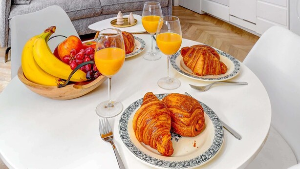 A modern kitchen with white cabinets and a dining area with a table set for breakfast. - Charming 1BR Near Eiffel Tower - Sleeps 4 (Paris)