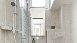 A modern bathroom with a glass-enclosed shower, a white toilet, and a vanity with a mirror and sink. - Charming 1BR Near Eiffel Tower - Sleeps 4 (Paris)
