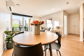 A modern living room with a round wooden table, black chairs, a sofa, and a large window with a view.