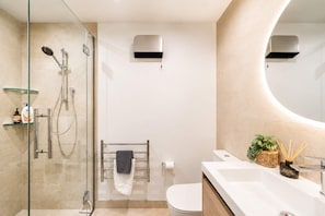 A modern bathroom with a glass shower enclosure, a toilet with a towel rack, and a sink with a mirror.