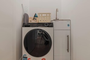 A compact, wall-mounted washer and dryer unit with a control panel, a circular door, and a small sink.