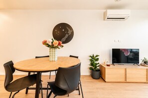 A modern living room with a round wooden dining table, black chairs, a round black wall art piece, a flat-screen TV on a wooden stand, and a potted plant. - Central 1BR Apartment | Full Kitchen + Patio (Christchurch)