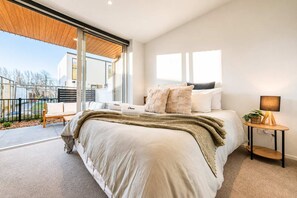A modern bedroom with a large bed, a bedside table with a lamp, and a view of the outdoors through a sliding door. - Central 1BR Apartment | Full Kitchen + Patio (Christchurch)