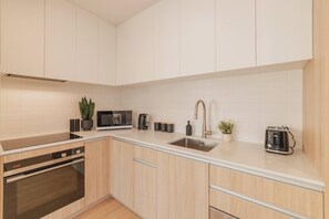 A modern kitchen with light wood cabinets, a stainless steel sink, a microwave, a toaster, and a coffee maker.
