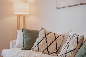 A white sofa with a blanket and three patterned cushions.