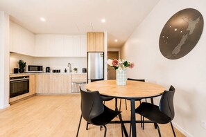 A modern kitchen with white cabinets, a stainless steel refrigerator, and a wooden dining table with four chairs. - Central 1BR Apartment | Full Kitchen + Patio (Christchurch)