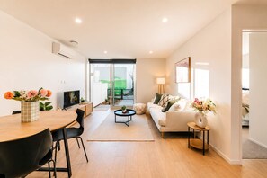 A modern living room with a dining area, a sofa, and a TV. - Central 1BR Apartment | Full Kitchen + Patio (Christchurch)