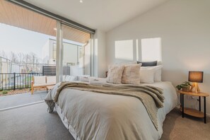 Un dormitorio moderno con una cama grande, una mesita de noche con lámpara y vistas al balcón exterior.