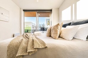 Une chambre à coucher avec un lit, des oreillers, une couverture, une fenêtre et une vue sur l’extérieur.