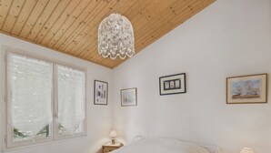 A bedroom with a wooden ceiling, a bed with white bedding, a nightstand with a lamp, and three framed pictures on the wall. - House in Les Conches, garden, sleeps 4 (Longeville-sur-Mer)