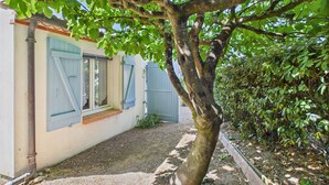 A tree in front of a building with blue shutters and a gravel path. - House in Les Conches, garden, sleeps 4 (Longeville-sur-Mer)
