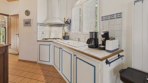 A kitchen with white cabinets, a stove, a coffee maker, and a window with lace curtains. - House in Les Conches, garden, sleeps 4 (Longeville-sur-Mer)