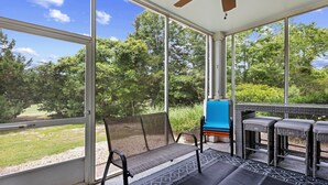 Eine überdachte Terrasse mit Tisch und Stühlen, ein blauer Stuhl sowie Blick auf eine grüne Fläche mit Bäumen.