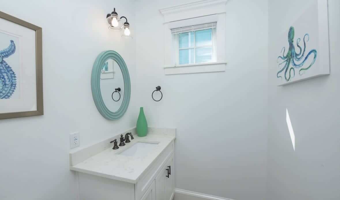 A bathroom with a white sink, a green vase, and framed artwork on the walls.
