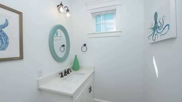 A bathroom with a white sink, a green vase, and framed artwork on the walls.