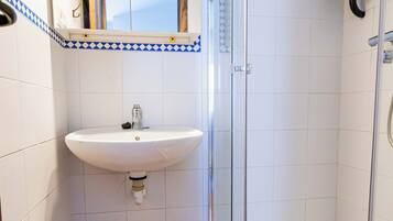 A bathroom with a white sink, a mirror, and a shower enclosure.