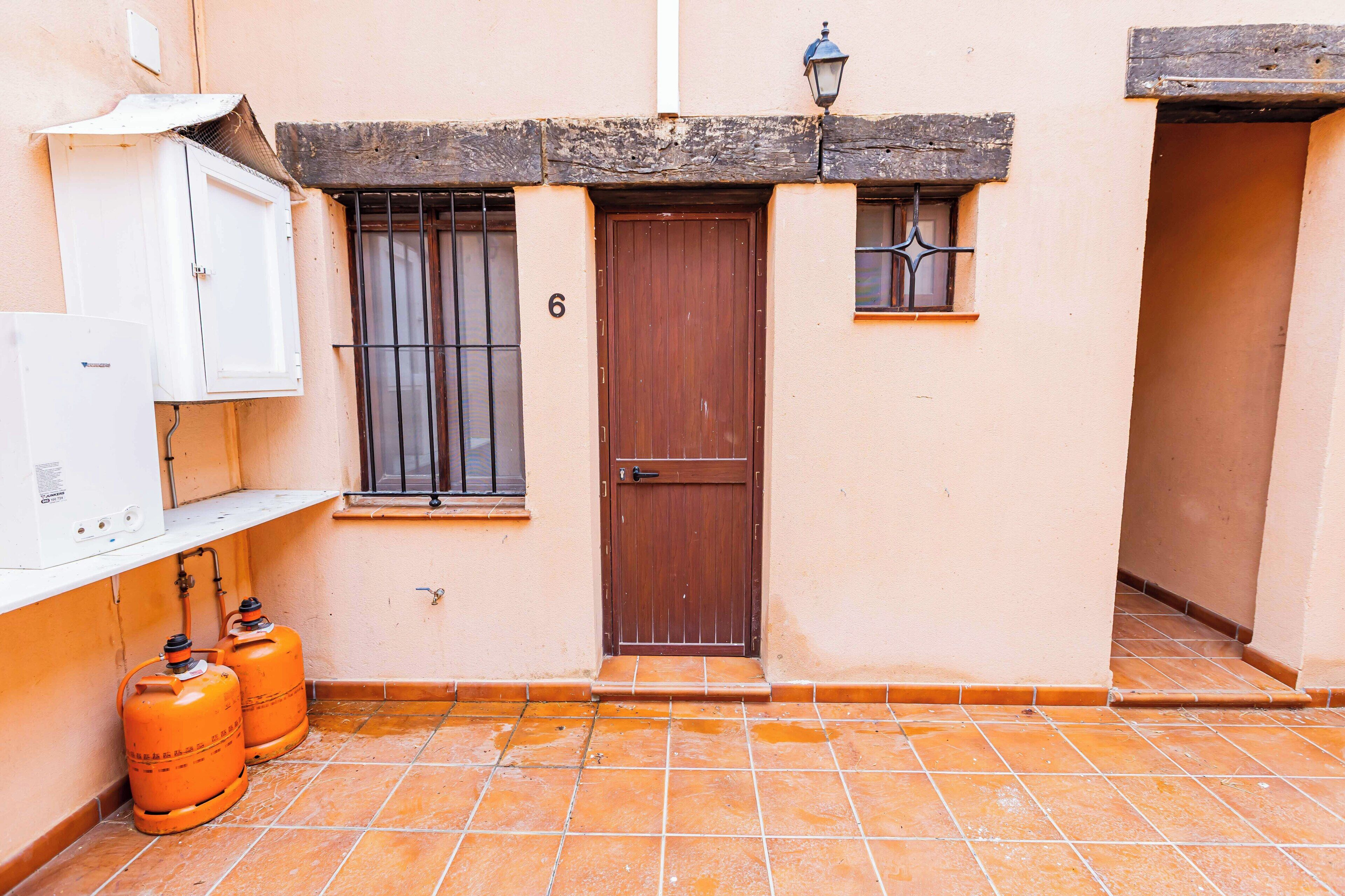 Un edificio con una puerta marrón, una ventana con barrotes y dos cilindros de gas naranja.