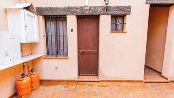 Un edificio con una puerta marrón, una ventana con barrotes y dos cilindros de gas naranja.