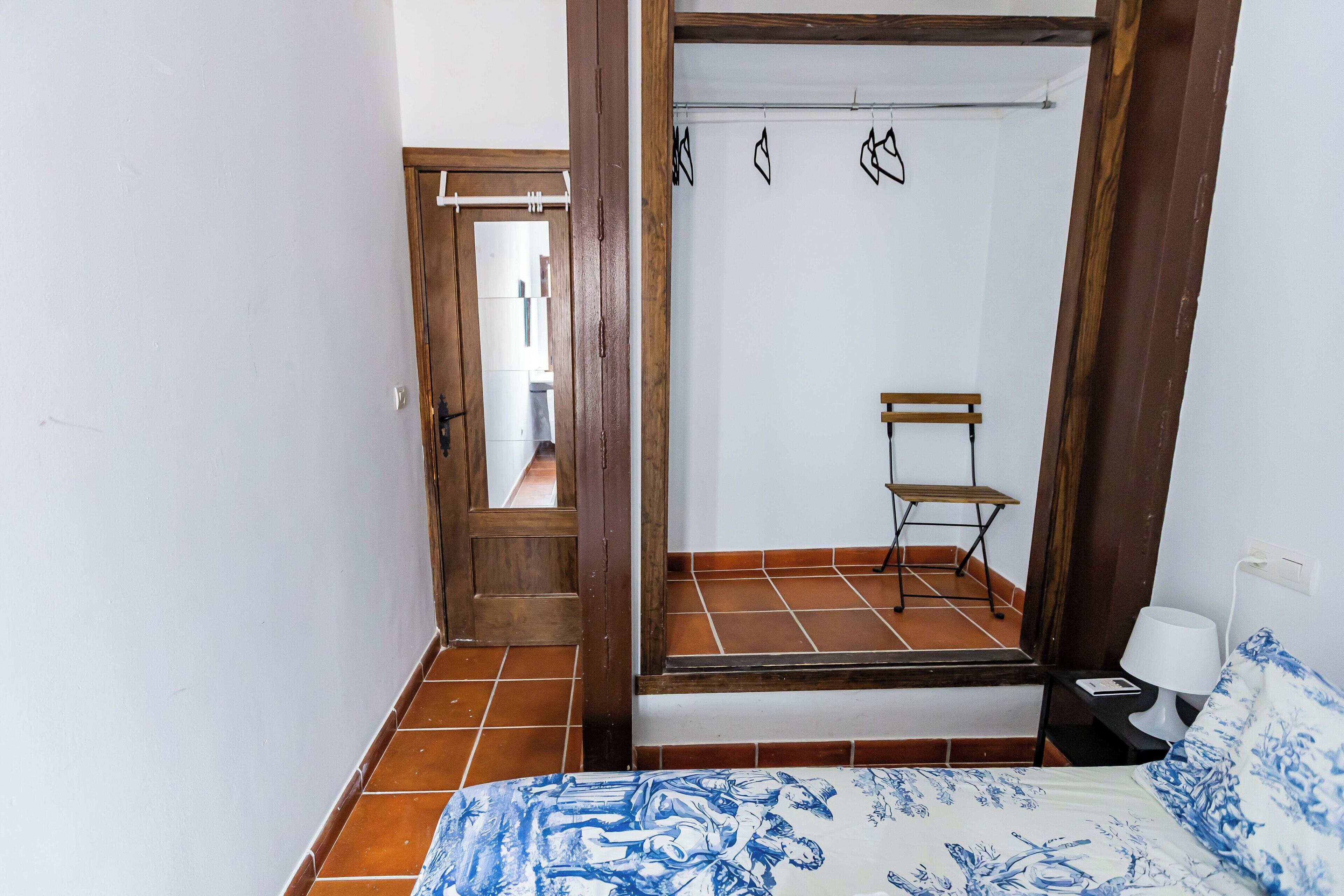 Un dormitorio con una cama, un armario de madera, una mesita de noche con lámpara y una silla.