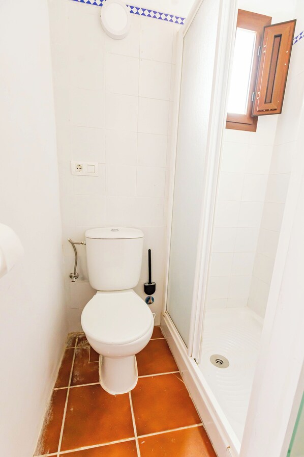 Un baño con inodoro, ducha y una ventana pequeña.
