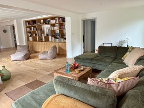 Un salon avec un canapé vert, un fauteuil poire, une table basse en bois et une bibliothèque remplie de livres.