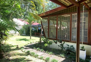 A covered outdoor area with a patio, a small garden with various plants, and a building with large windows.