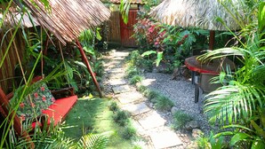 A tropical garden with thatched-roof structures, a stone pathway, and lush greenery. - Villa #2 - 1 Bedroom with private Garden (Puerto Viejo de Talamanca)