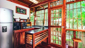 A kitchen with wooden cabinets, a stainless steel refrigerator, a sink, and a window with a view of greenery. - Villa #2 - 1 Bedroom with private Garden (Puerto Viejo de Talamanca)