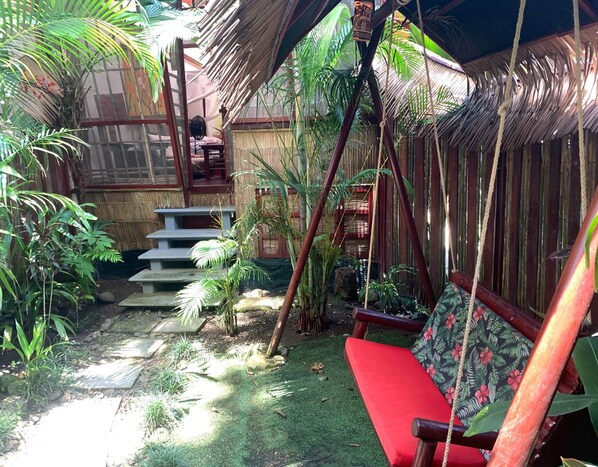 A tropical garden with a hammock, stone steps, and a thatched-roof structure.