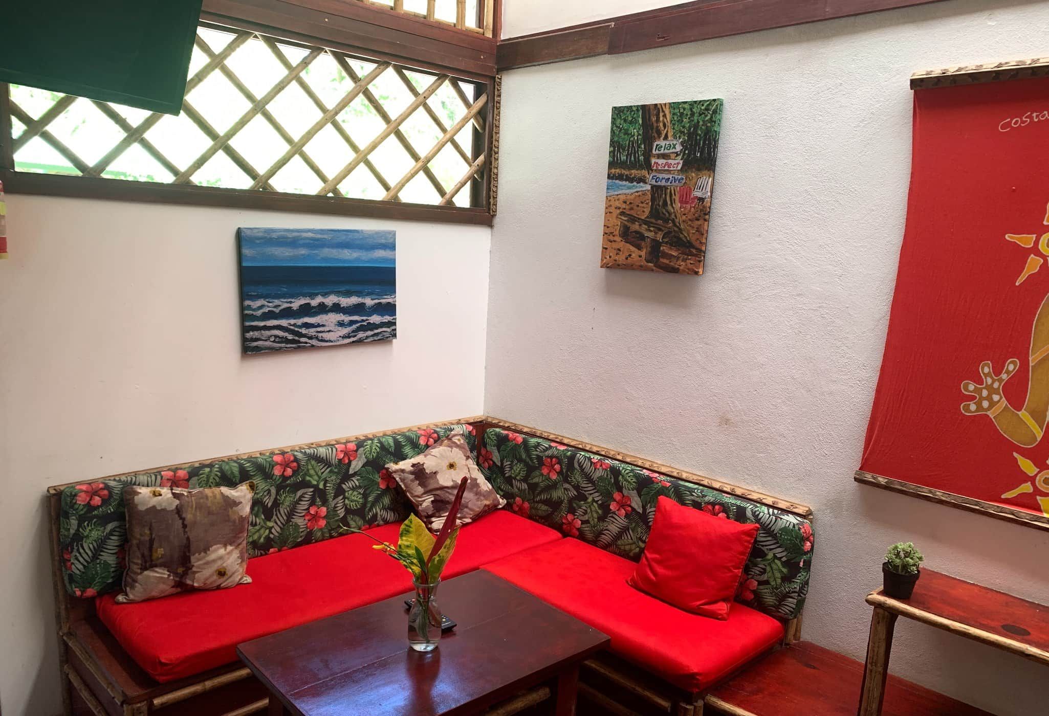A room with a corner sofa, a table with a vase, and artwork on the walls.